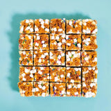 Cereal Milk Rocky Road squares topped with crunchy cornflakes, malted marshmallows, and rainbow sprinkles by Crumbs & Doilies